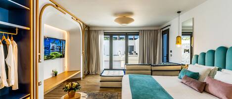 A modern hotel room with a large bed, a seating area, a TV, and a view of the outdoors.