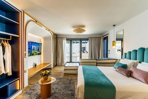 A modern hotel room with a large bed, a seating area, a TV, and a view of the outdoors.