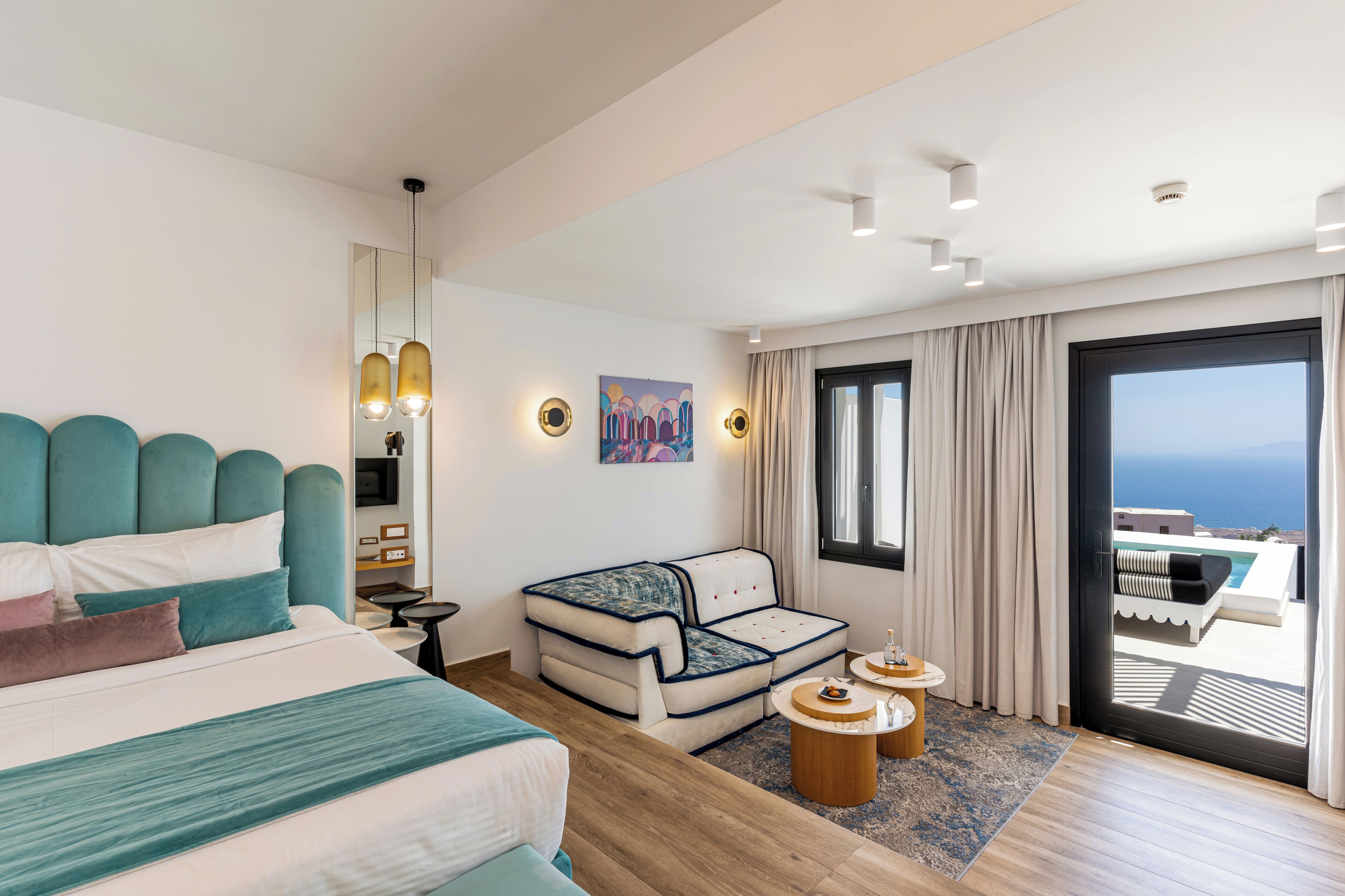 Una habitación de hotel moderna con una cama grande, un sofá, una mesita y vista al océano.