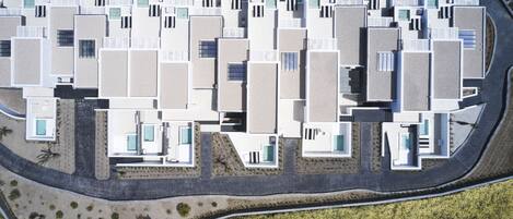 An aerial view of a modern hotel with multiple rectangular buildings, each with balconies and swimming pools.