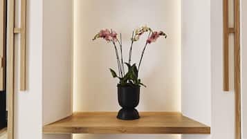 Um interior moderno com um banco de madeira, um vaso preto com orquídeas e uma parede branca com detalhes em madeira.