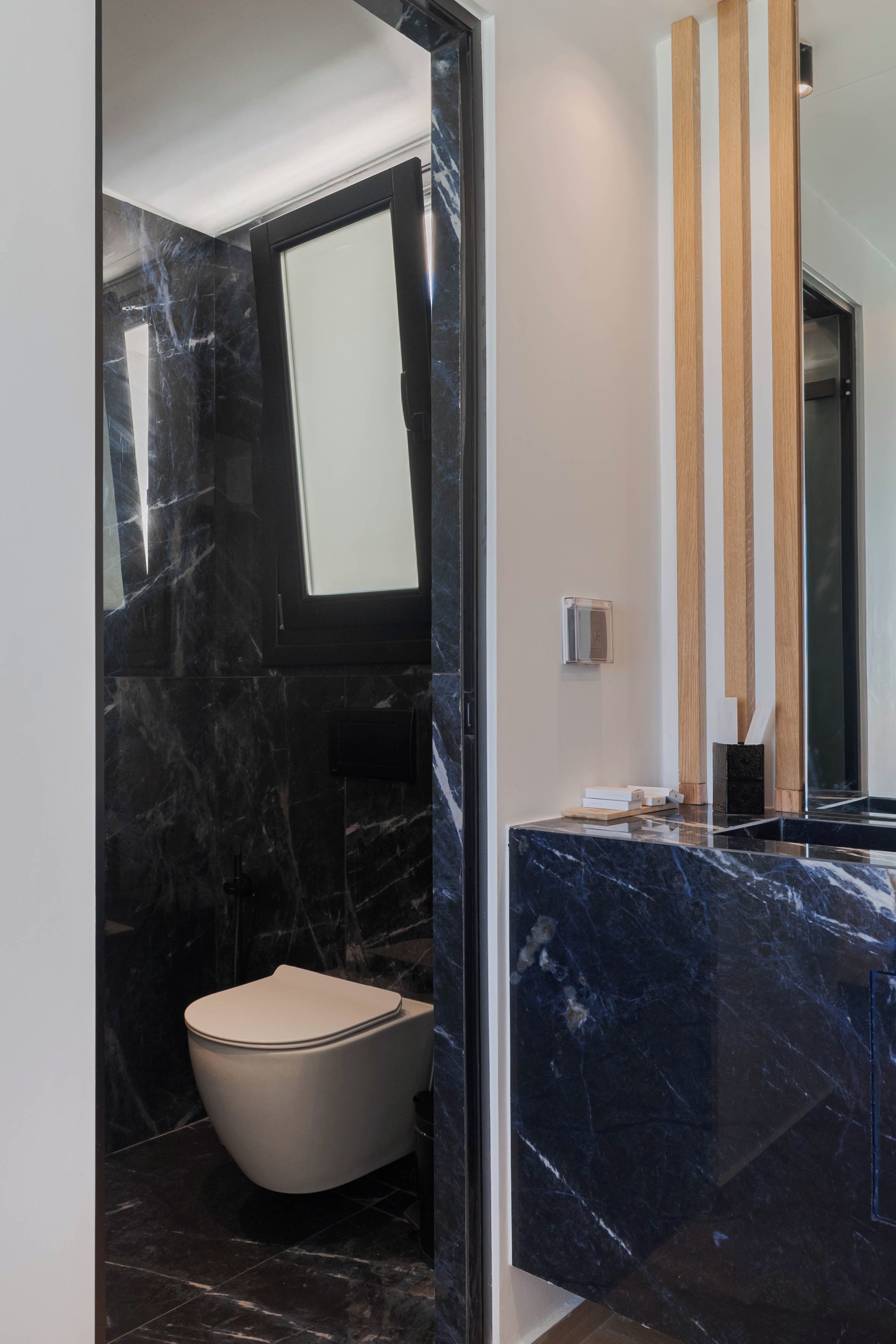 A modern bathroom with a marble floor, a toilet, and a vanity with a mirror.