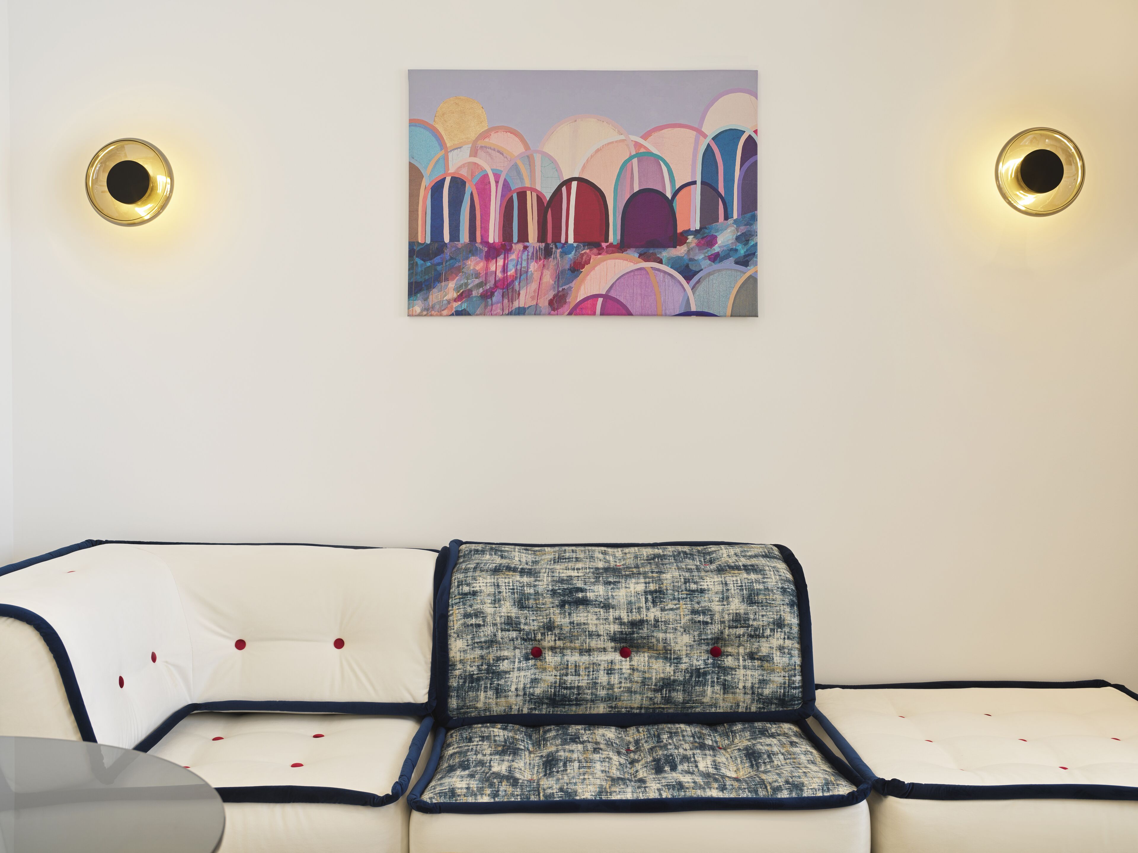 A modern living room with a white sofa, a blue and white patterned throw pillow, and a colorful abstract painting on the wall.