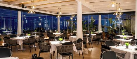 Un restaurant avec des tables rondes, des chaises en osier et des lampes suspendues.