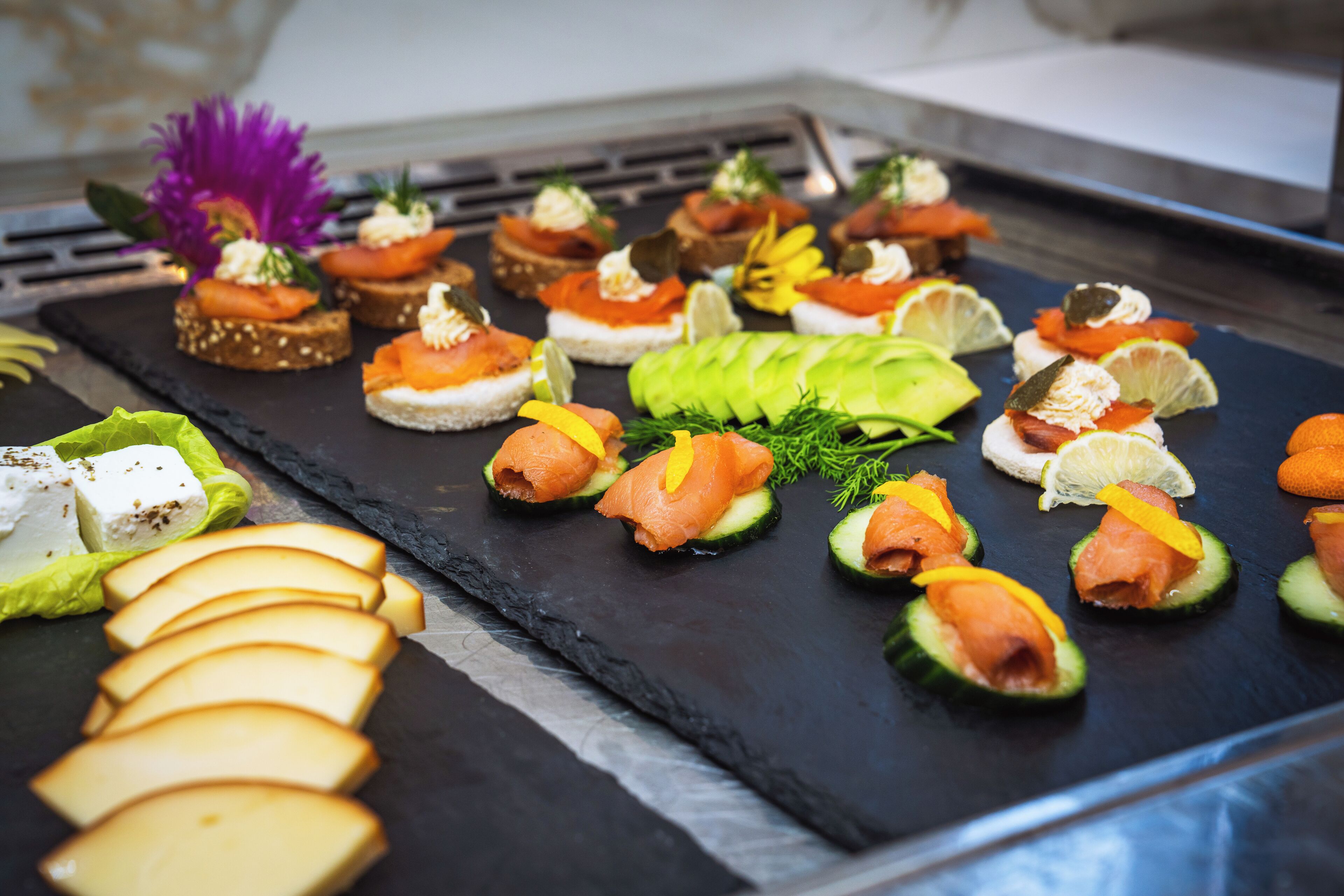 A variety of appetizers on a slate board, including smoked salmon, cream cheese, and avocado slices.