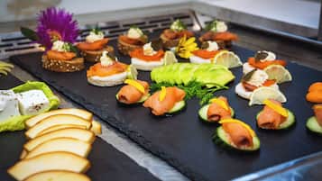 Diverse hapjes op een leistenen plank, waaronder gerookte zalm, roomkaas en avocado plakjes.