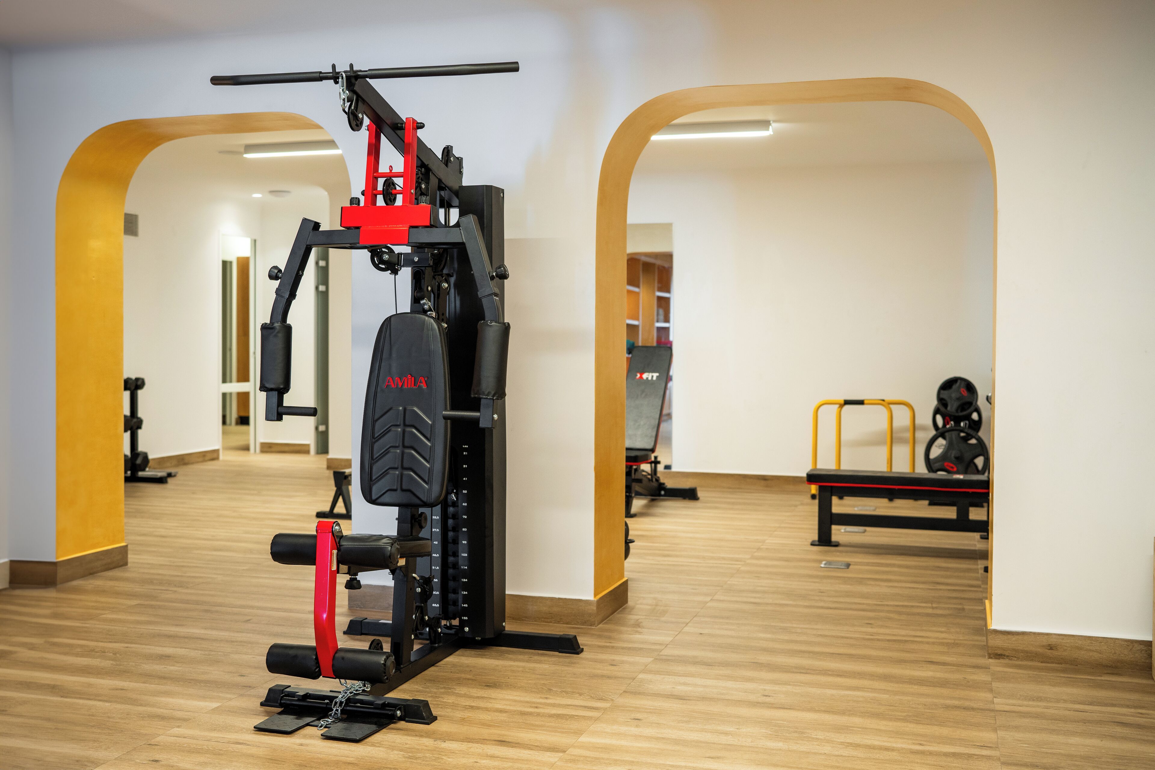 Un gimnasio con equipamiento de levantamiento de pesas, suelo de madera y diseño con arcos abiertos.