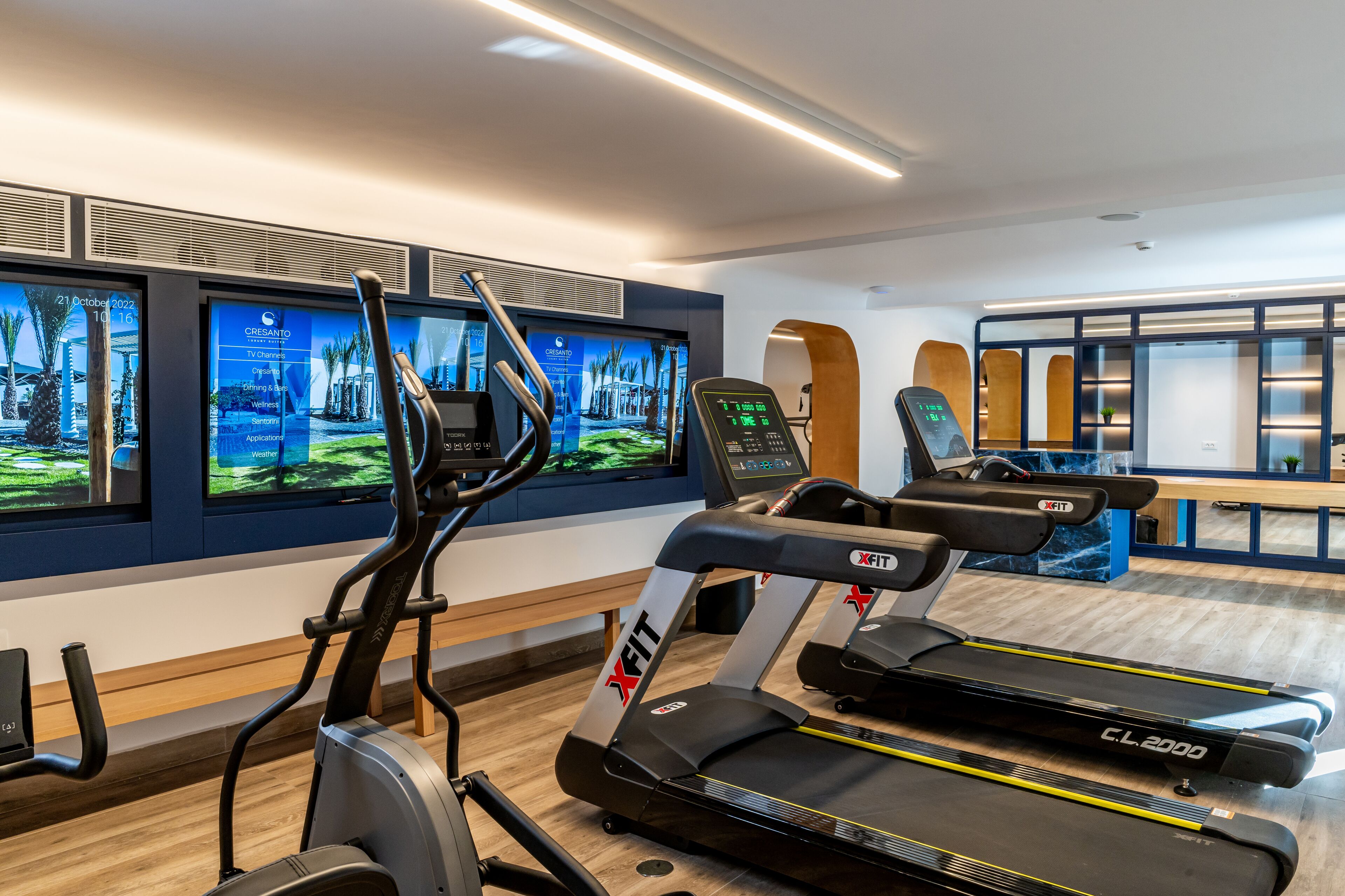 A modern gym with treadmills, an elliptical, and a TV displaying fitness programs.