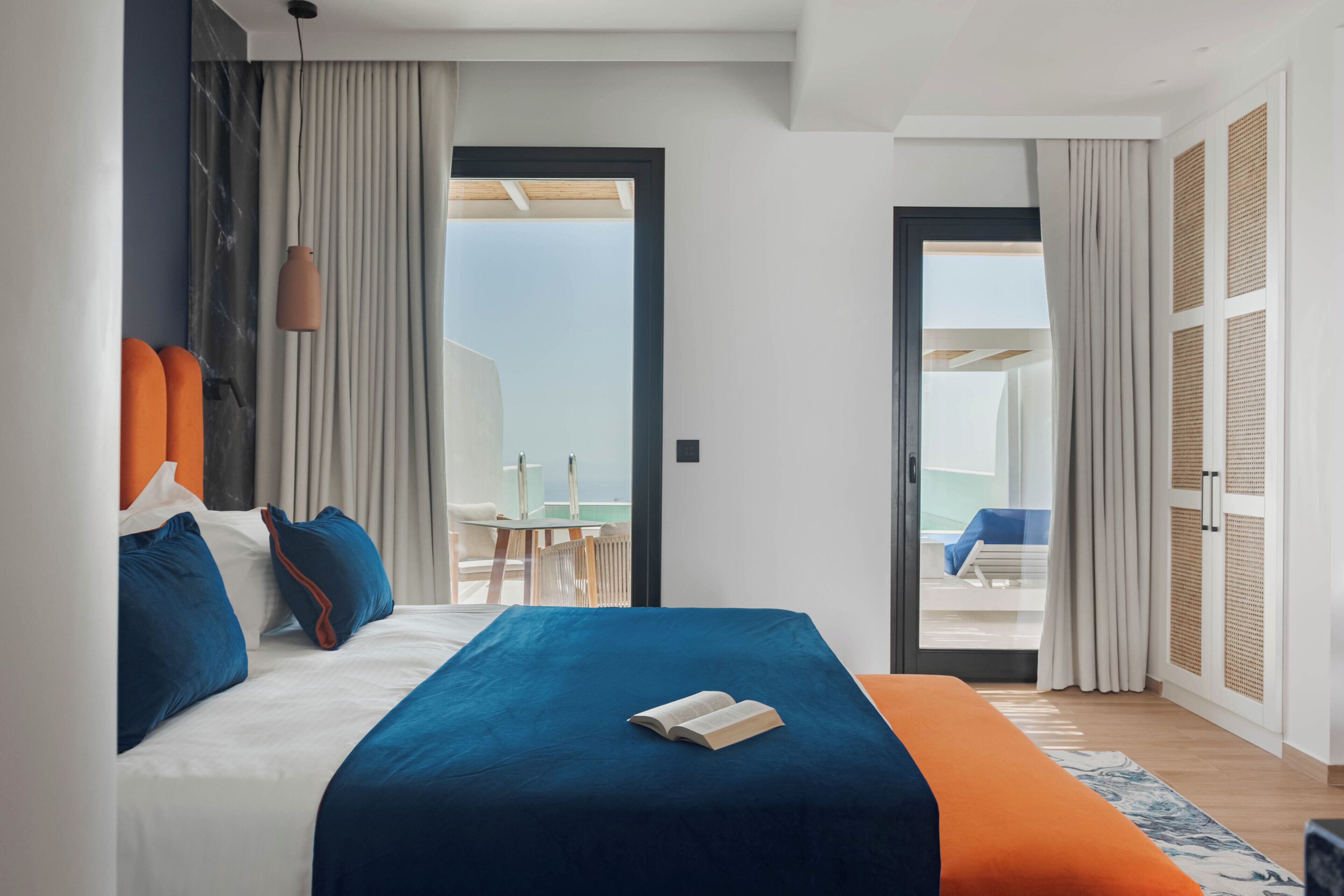 A modern hotel room with a large bed, a balcony, and a view of the sky.