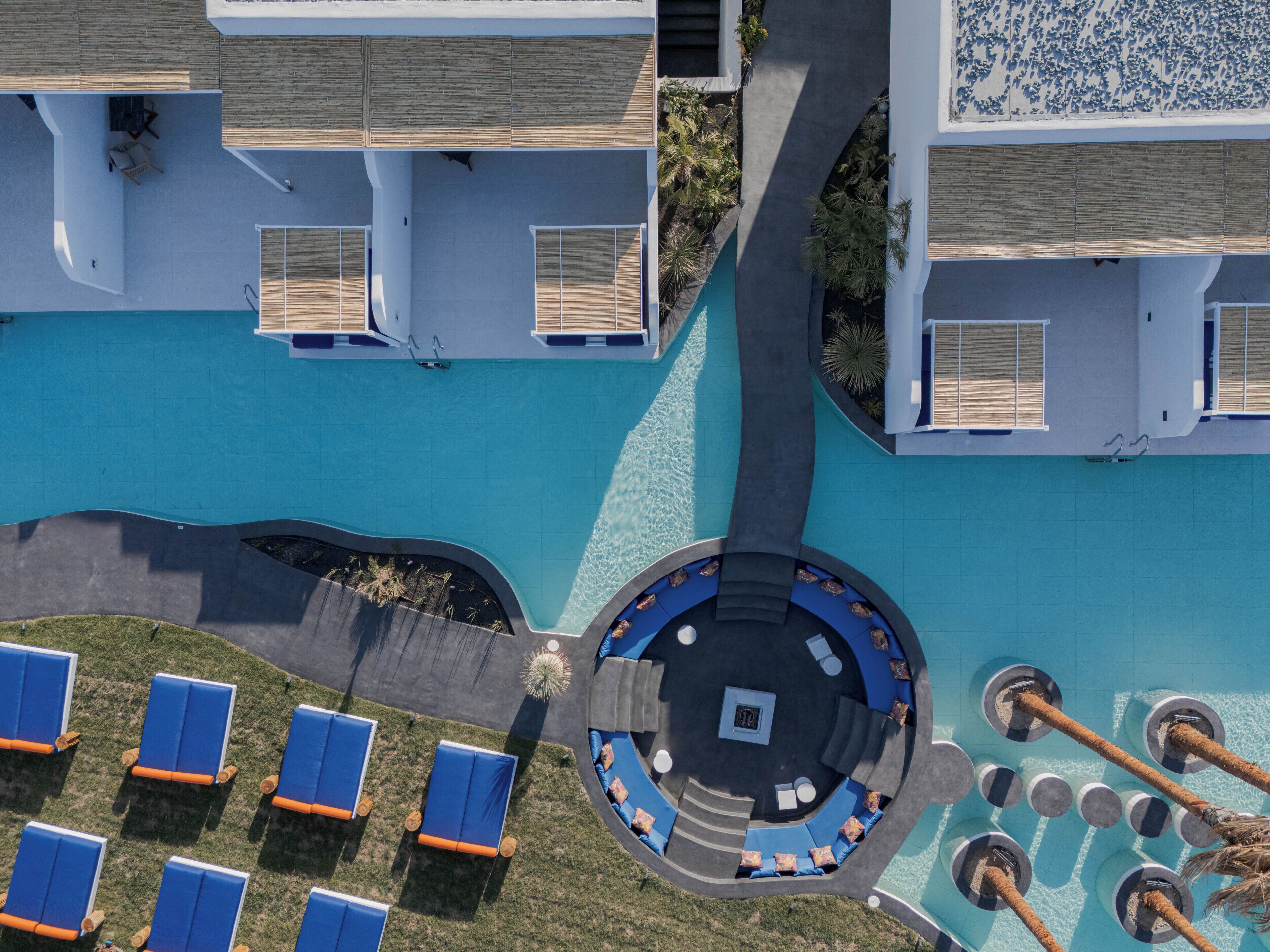 An aerial view of a resort with a swimming pool, lounge chairs, and a circular seating area.
