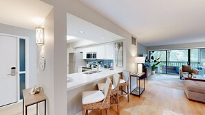 A modern kitchen with white cabinets, a central island, and a dining area with wicker chairs. - Stunning, coastal chic two bedroom, two bathroom villa in Palmetto Dunes!! (Hilton Head)
