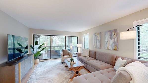 A spacious living room with a large TV, comfortable seating, and a view to the outside. - Stunning, coastal chic two bedroom, two bathroom villa in Palmetto Dunes!! (Hilton Head)