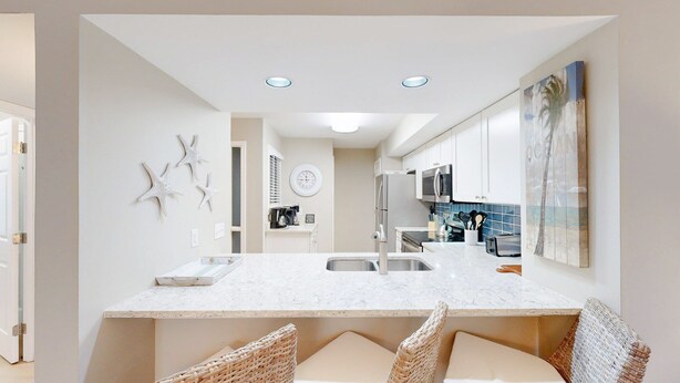 A modern kitchen with white cabinetry, a marble countertop, and a central island with seating. - Stunning, coastal chic two bedroom, two bathroom villa in Palmetto Dunes!! (Hilton Head)