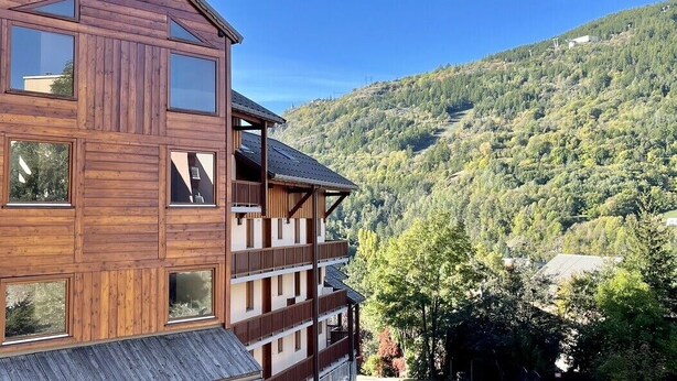 A multi-story wooden building with balconies, set against a mountainous backdrop. - Nice Cosy Apt With Balcony In Briançon (Briançon)