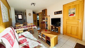 A cozy living room with a sofa, wooden TV stand, and a dining area with a table and chairs. - Nice Cosy Apt With Balcony In Briançon (Briançon)