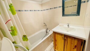 A bathroom with a bathtub, a sink, wooden cabinets, and a mirror. - Nice Cosy Apt With Balcony In Briançon (Briançon)