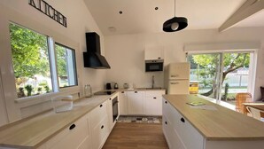 A modern kitchen with white cabinetry, a black range hood, and a large window providing natural light.