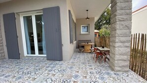 A covered patio with patterned flooring, a table with chairs, and a wooden fence.