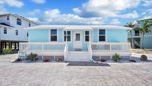 A two-story house with a white porch and a blue roof, surrounded by a sandy landscape. - 🌊Updated Vintage Beach House-Private Pool, Steps to Beach-Blue Lizard🦎 (Fort Myers Beach)
