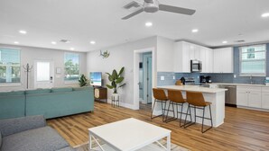 A modern kitchen with white cabinets, a central island with bar stools, and a ceiling fan. - 🌊Updated Vintage Beach House-Private Pool, Steps to Beach-Blue Lizard🦎 (Fort Myers Beach)