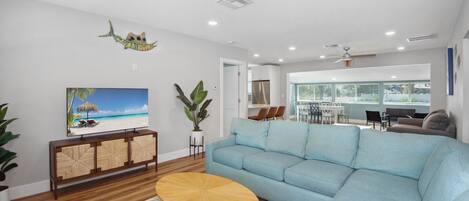 A modern living room with a light blue sofa, a wooden coffee table, and a TV displaying a beach scene.