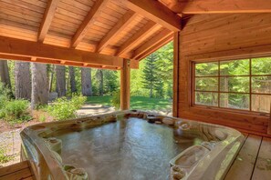 Een houten blokhut met een jacuzzi en een groot raam met uitzicht op een bebost gebied.