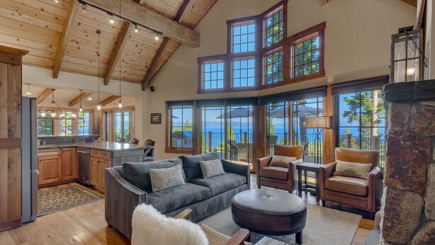Amplia sala de estar con techo alto, vigas de madera, chimenea y ventanas grandes con vistas al exterior.