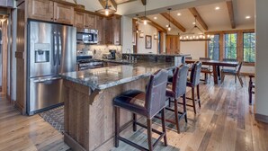 Una cocina amplia con una isla grande, armarios de madera, electrodomésticos de acero inoxidable y un comedor con taburetes de bar.