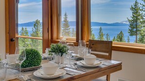 A dining table set for four with a scenic view of mountains and a lake through large windows. - Sierra Vista - Lakeview - TLUXP (Tahoe City)