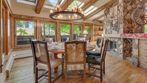 Un espace repas comprenant une table et des chaises en bois, une cheminée en pierre et de grandes fenêtres.