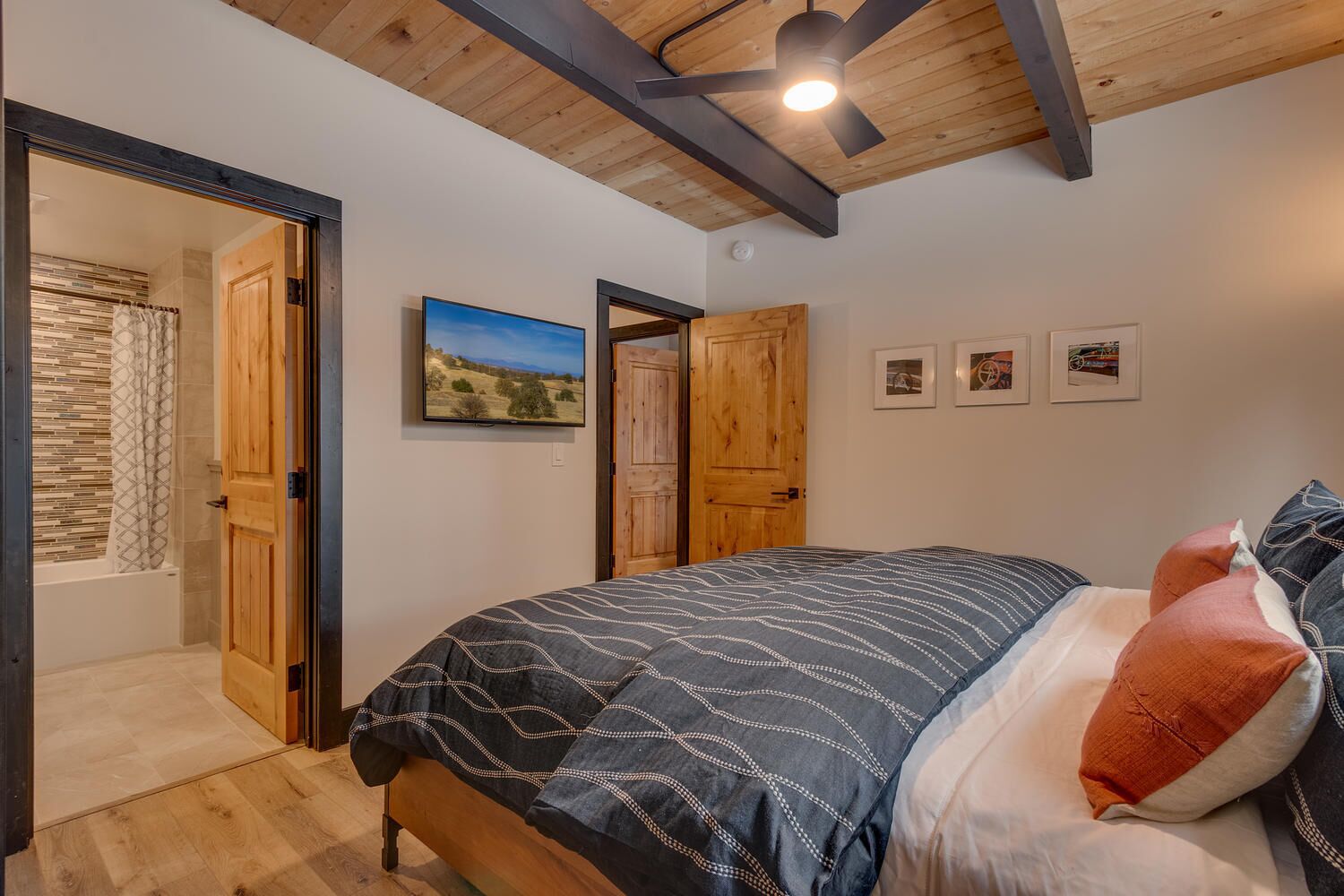 Un dormitorio con cama, vigas de madera en el techo, ventilador de techo y un ventanal grande.