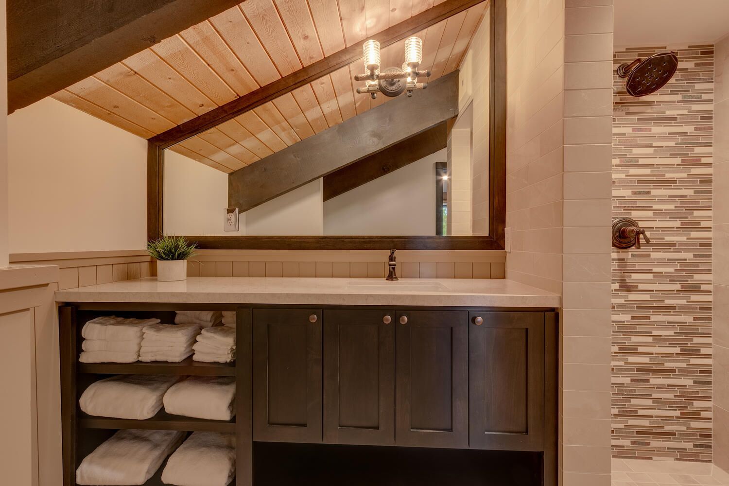 A bathroom with a wooden ceiling, a mirror, a sink, and a towel rack.