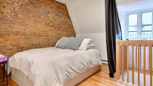 Ein Schlafzimmer mit Backsteinwand, einem hölzernen Bett, einem Fenster mit Vorhängen und einem Holzgeländer.