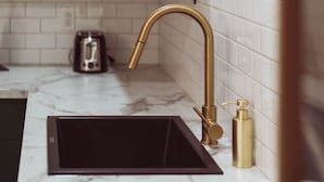 Eine Küche mit weißen, im Zementstil gehaltenen Fliesen, einem goldenen Wasserhahn und einer schwarzen Spüle.