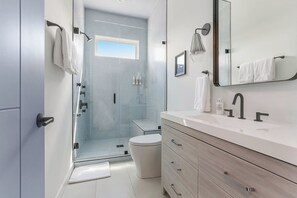 A modern bathroom with a shower, toilet, vanity, and a large mirror.