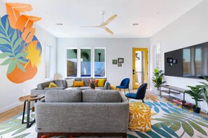 A modern living room with a grey sofa, blue chairs, a wooden coffee table, and a large TV.