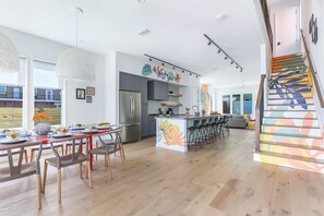 A modern kitchen with a central island, a dining area with a red table, and a staircase with colorful steps.