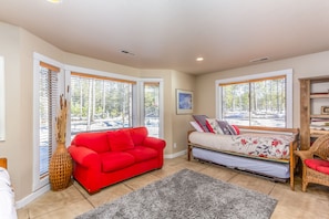 A room with a red sofa, a bed with floral bedding, a grey rug, and large windows with blinds.