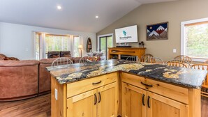 A kitchen with wooden cabinets and a granite countertop, a dining area with wooden chairs, and a living room with a brown sofa. - BLUE01 - Spacious Home, AC, SHARC Passes, Hot Tub (Sunriver)