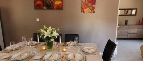 Un coin repas avec une table dressée pour six personnes, des chaises noires et un vase rempli de fleurs.