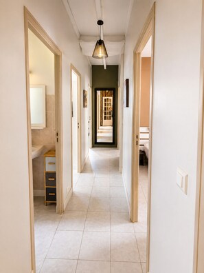 Un couloir avec un luminaire, une porte donnant sur une salle de bain et un escalier.