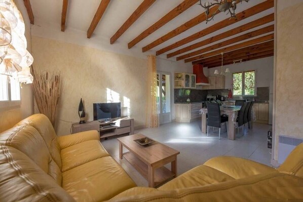 A living room with a sofa, a coffee table, and a TV. There is a kitchen area with cabinets and a dining table. - Charming country house between lot and dordogne (Salviac)