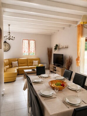 Un coin repas avec une table dressée pour quatre personnes, un canapé, un téléviseur et une fenêtre avec des rideaux.