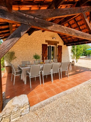 An outdoor patio with a brick wall, wooden beams, and a table set for dining.