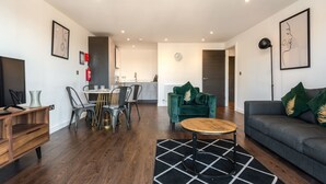 A modern living room with a sofa, a coffee table, and a dining area with chairs and a table. - Stay Zeni – Contemporary 2 BR Flat in York, Ouse Court (York)