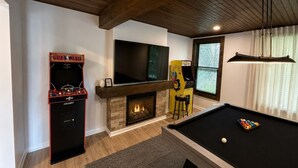 Ein Raum mit Billardtisch, Kamin, Fernseher und Spielautomaten.