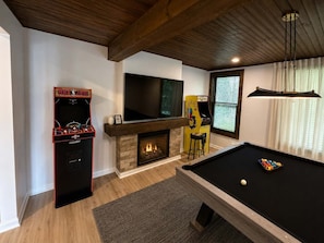 A room with a pool table, a fireplace, a television, and arcade games.