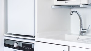 Een kleine keuken met een wasmachine, een magnetron en een spoelbak.