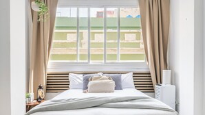 Een slaapkamer met een bed, een nachtkastje met een lamp en een raam met gordijnen.