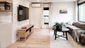 A modern living room with a wooden floor, a sofa, a coffee table, and a TV mounted on the wall. - Black Pearl - Lake Placid, Mirror Lake (Lake Placid)